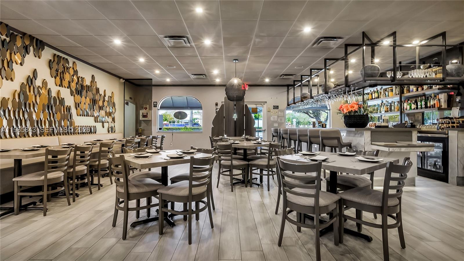 A restaurant dining room features gray wood-look flooring, a bar area, and decorative wall art — 2220 N University Dr, Sunrise FL 33322, SUNRISE, FL