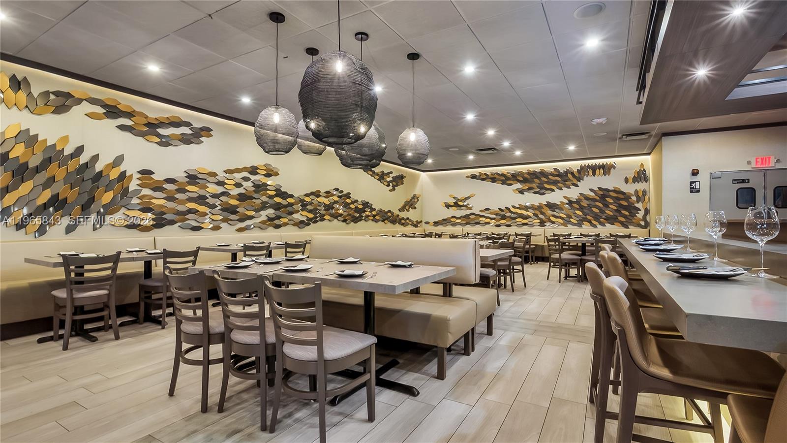 A restaurant dining room features booth seating, wooden chairs, pendant lights, and wall-mounted geometric decor — 2220 N University Dr, Sunrise FL 33322, SUNRISE, FL