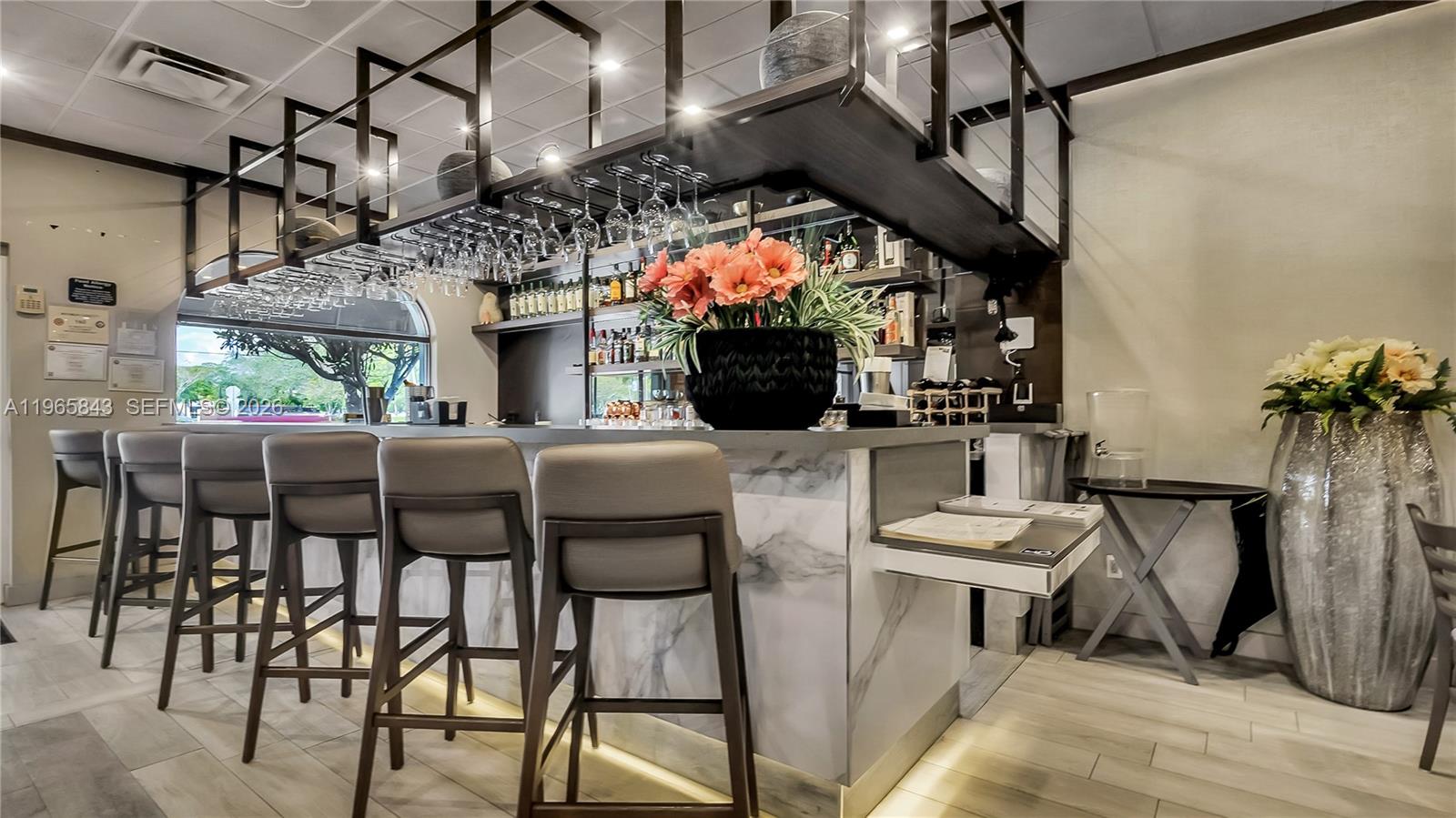 A modern bar area features marble-topped counters, gray stools, and a suspended metal glass rack — 2220 N University Dr, Sunrise FL 33322, SUNRISE, FL