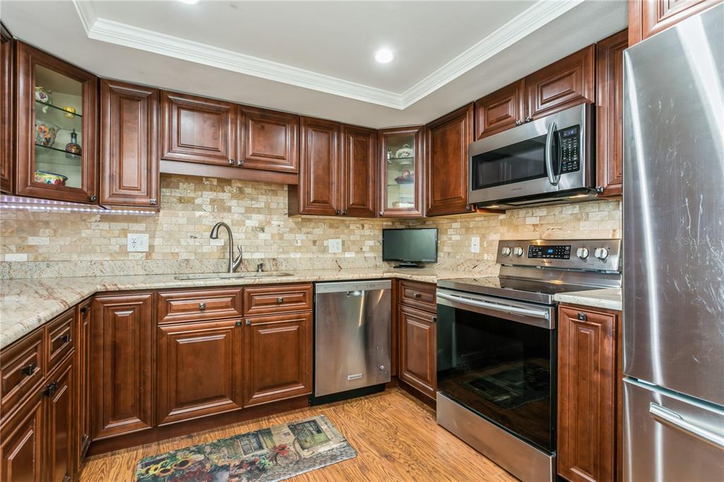 A kitchen featuring dark wood cabinets, stainless steel appliances, and a stone tile backsplash — 5200 BRITTANY DRIVE S UNIT 1708, ST PETERSBURG, FL