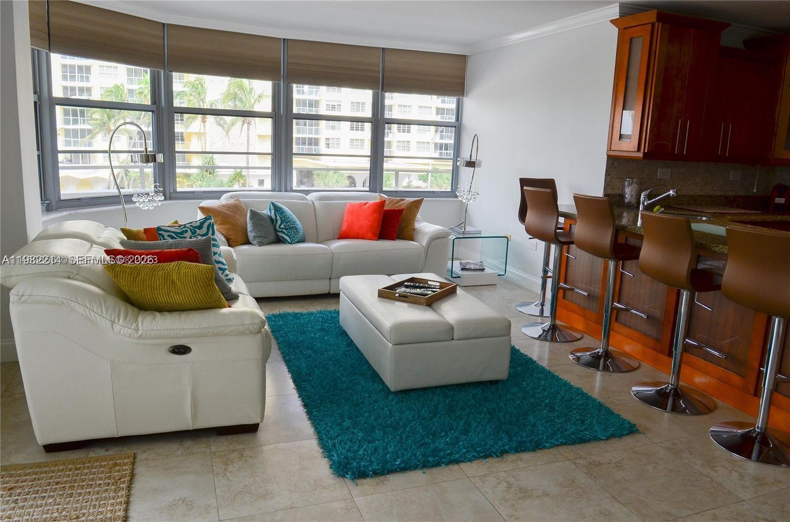 A living room features white leather sofas, a teal shag rug, and a kitchen breakfast bar — 5555 Collins Ave # 4A, Miami Beach FL 33140, MIAMI BEACH, FL