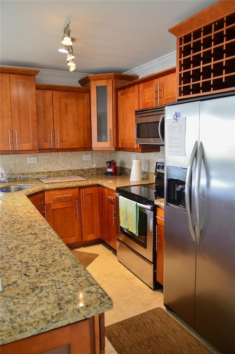 A kitchen features wooden cabinets, granite countertops, and stainless steel appliances — 5555 Collins Ave # 4A, Miami Beach FL 33140, MIAMI BEACH, FL