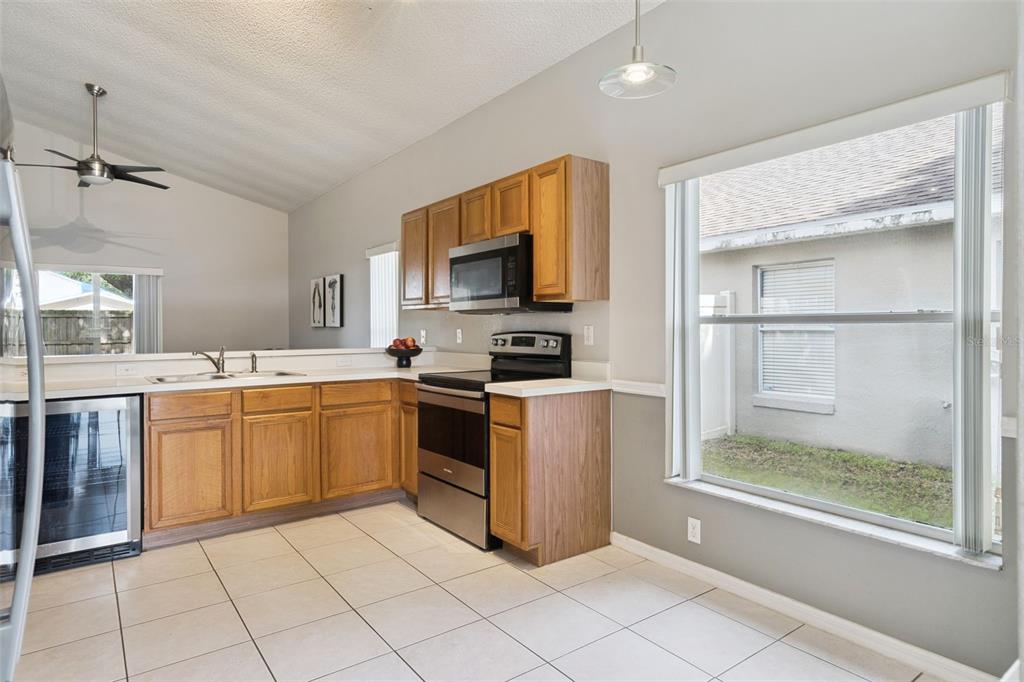 A kitchen with oak cabinets, stainless steel appliances, tile flooring, and a large window — 2712 BIRMINGHAM BOULEVARD, ORLANDO, FL