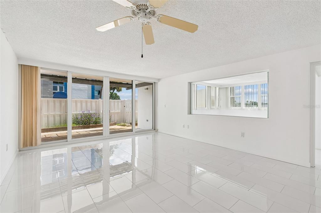 A bright, empty living room features white tile floors, a ceiling fan, and sliding glass doors — 450 TREASURE ISLAND CAUSEWAY UNIT 106, TREASURE ISLAND, FL