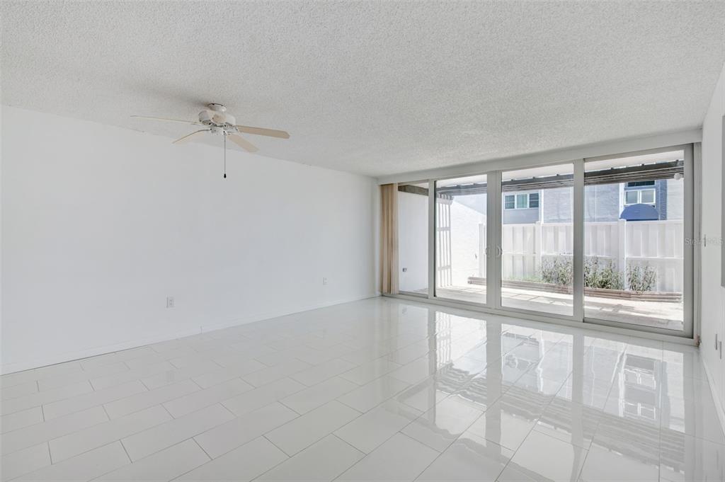 A bright, empty living room features white tile floors, a ceiling fan, and sliding glass doors — 450 TREASURE ISLAND CAUSEWAY UNIT 106, TREASURE ISLAND, FL
