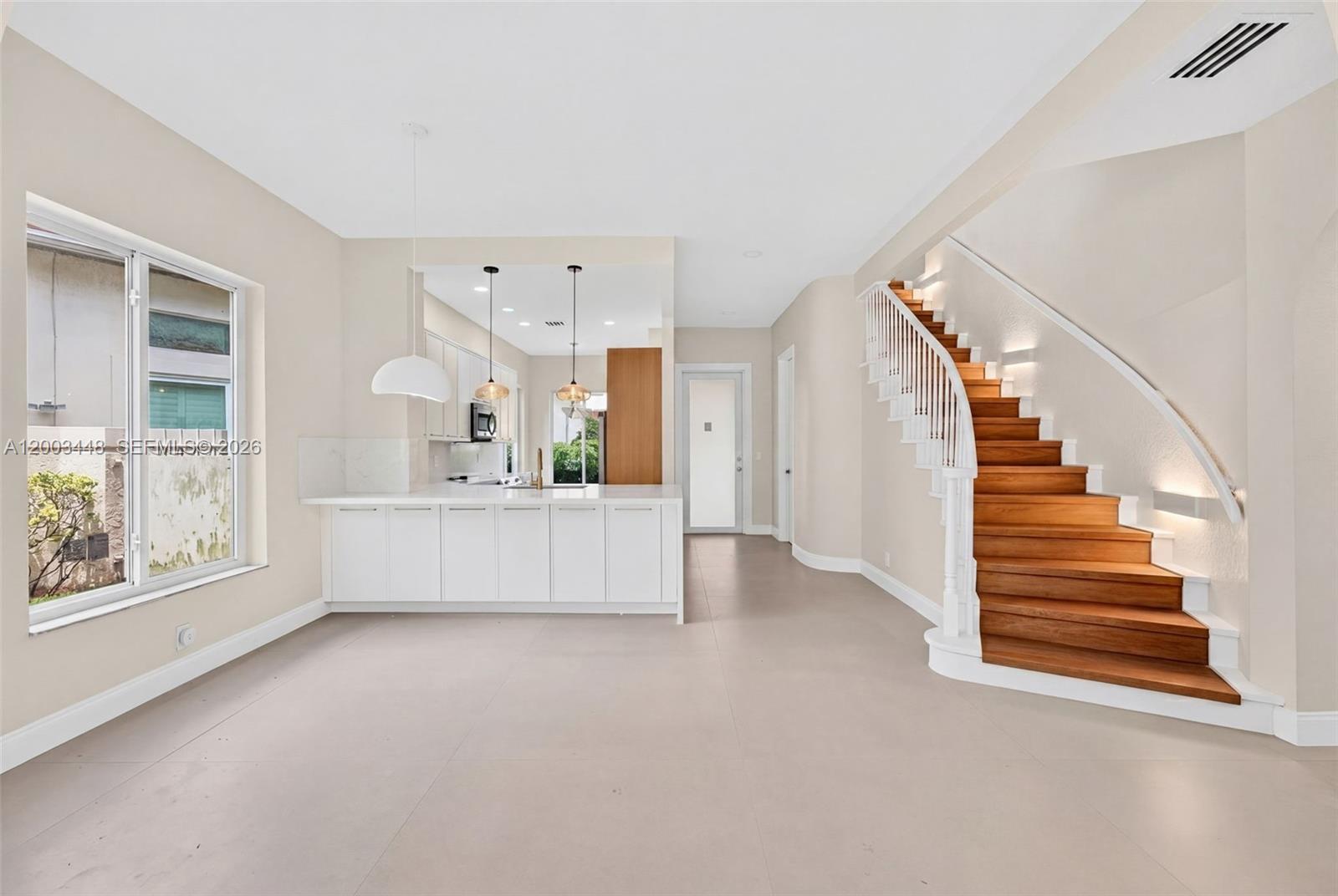 A modern kitchen with white cabinetry and a wooden staircase sits in an open room — 2546 NW 52nd St, Boca Raton FL 33496, BOCA RATON, FL
