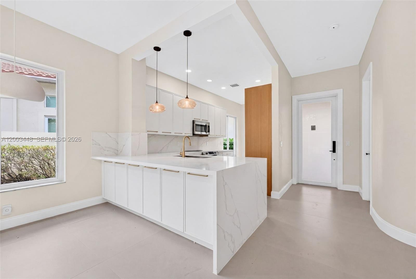 A modern kitchen features white cabinets, a marble waterfall island, and two pendant lights — 2546 NW 52nd St, Boca Raton FL 33496, BOCA RATON, FL