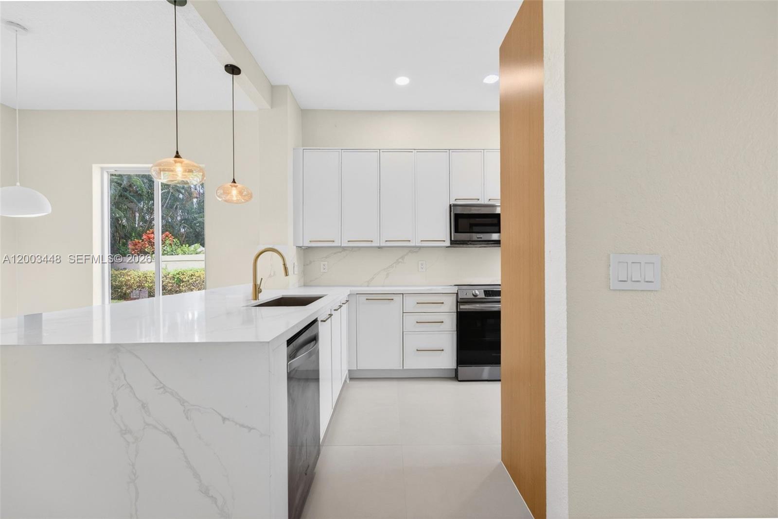A modern kitchen features white cabinets, a marble-patterned island, and gold-toned fixtures — 2546 NW 52nd St, Boca Raton FL 33496, BOCA RATON, FL