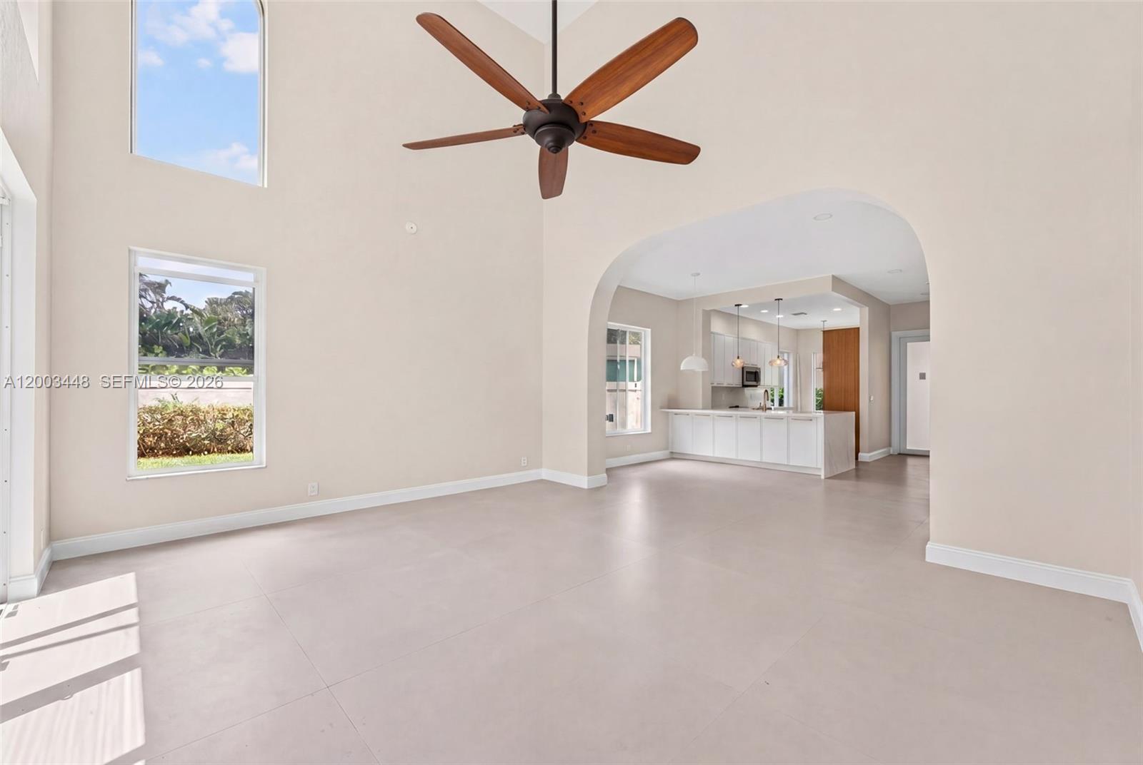 A spacious living room with high ceilings, a ceiling fan, and an arched kitchen entrance — 2546 NW 52nd St, Boca Raton FL 33496, BOCA RATON, FL