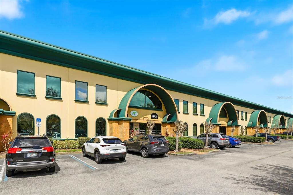 A low-rise commercial building with a green roofline and arched entrances sits above a parking lot — 6881 KINGSPOINTE PARKWAY UNIT 3, ORLANDO, FL