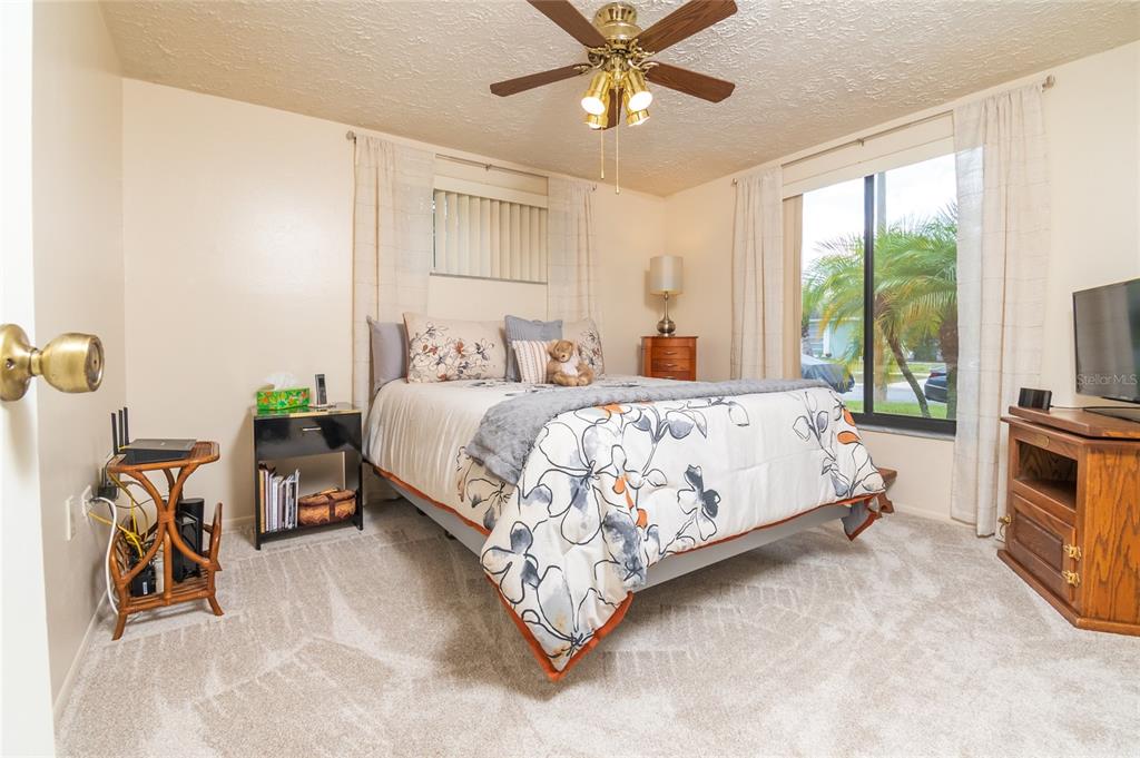 A bedroom features a bed with floral bedding, a ceiling fan, and a large window — 6710 RANCHWOOD LOOP, NEW PORT RICHEY, FL