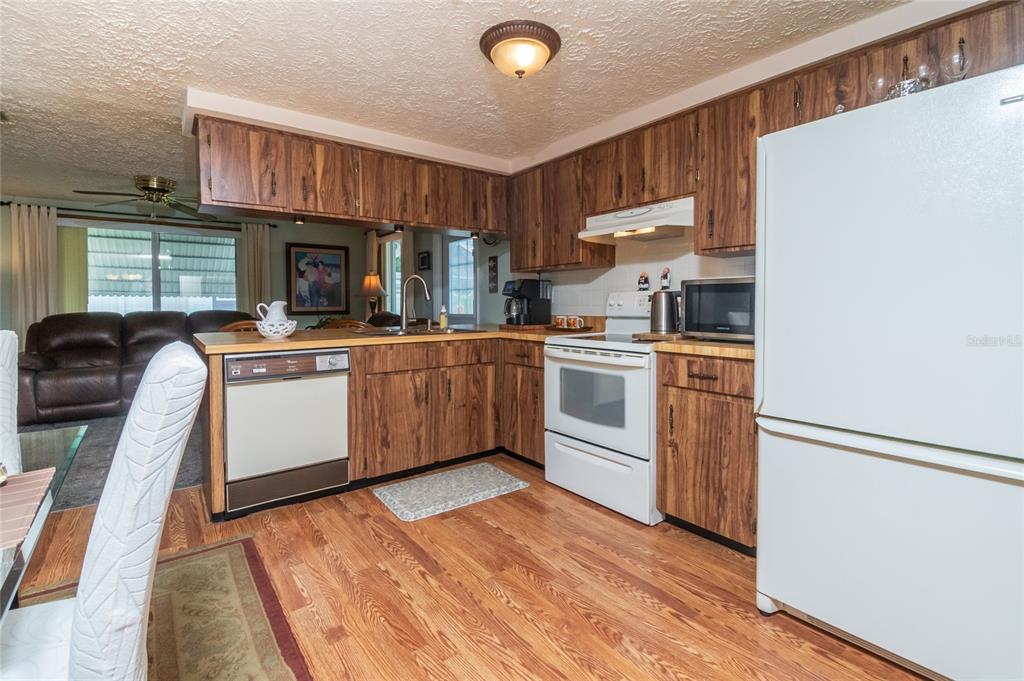 A kitchen features wood-grain cabinets, white appliances, and wood-look flooring, opening to a living area — 6710 RANCHWOOD LOOP, NEW PORT RICHEY, FL