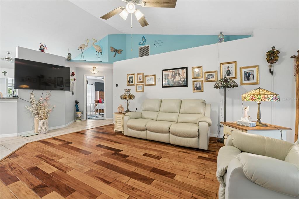 A living room features a light-colored sofa, wood flooring, and a vaulted ceiling with decor — 4025 S LINWOOD TERRACE, INVERNESS, FL