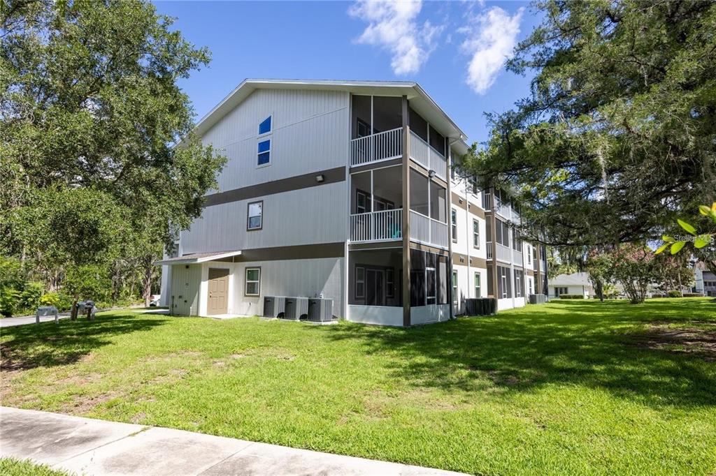 A three-story apartment building with screened balconies and a tan exterior sits on a lawn — 6519 W NEWBERRY ROAD UNIT 412, GAINESVILLE, FL
