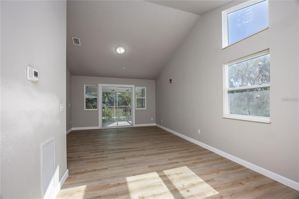 An empty living room features vaulted ceilings, light wood-look flooring, and a sliding glass door — 6519 W NEWBERRY ROAD UNIT 412, GAINESVILLE, FL