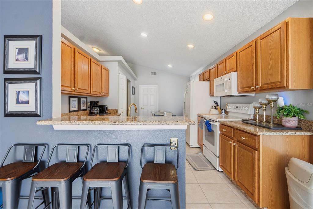A kitchen with wood cabinets, granite countertops, and a breakfast bar with metal stools — 334 BRAYTON LANE, DAVENPORT, FL