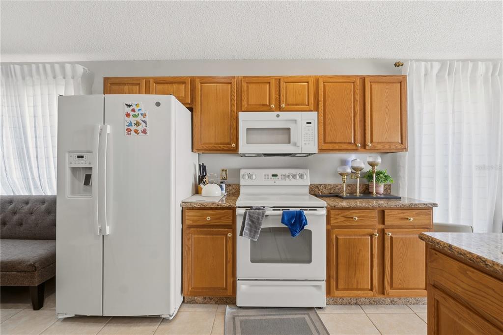 A kitchen features oak cabinets, white appliances, and a granite countertop against a light wall — 334 BRAYTON LANE, DAVENPORT, FL