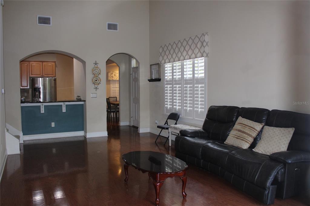 A living room with hardwood floors, a black leather sofa, and an arched kitchen entryway — 4961 ANNISTON CIRCLE, TAMPA, FL
