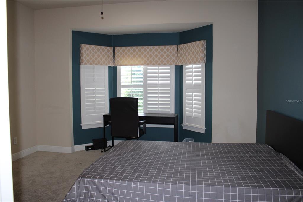 A bedroom features a bay window with shutters, a desk, and a bed with plaid bedding — 4961 ANNISTON CIRCLE, TAMPA, FL