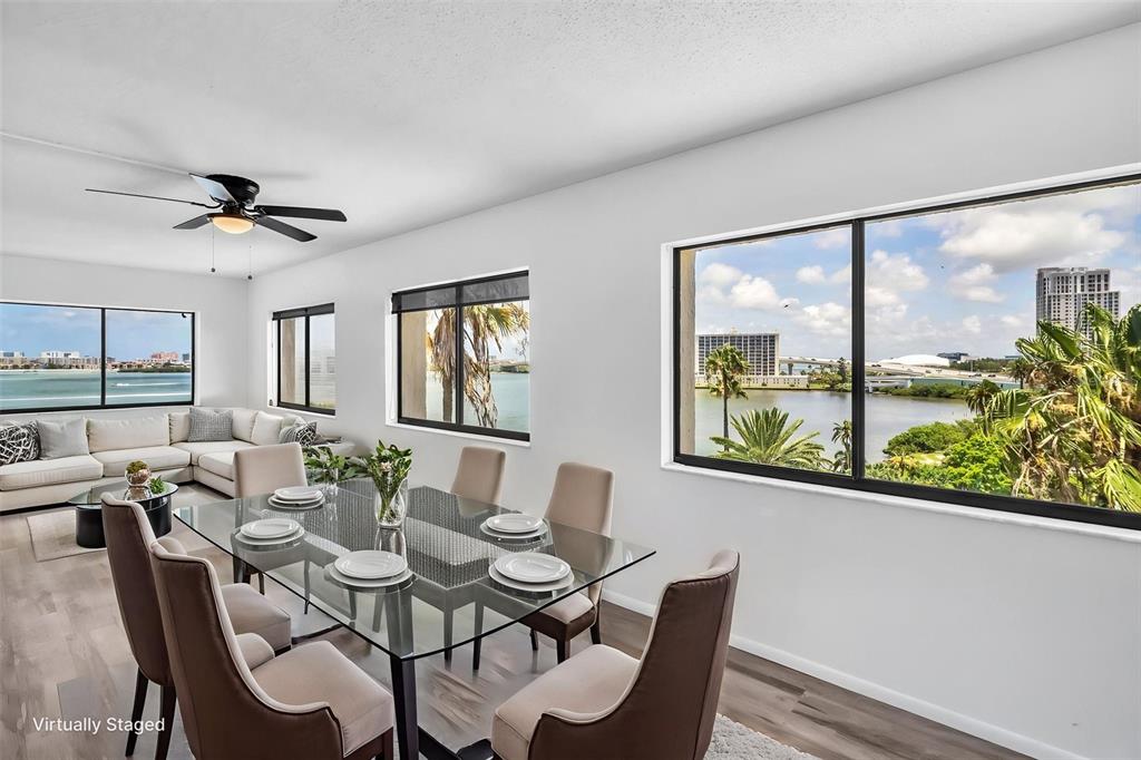A dining and living area features a glass table, neutral furniture, and large waterfront windows — 55 ROGERS STREET UNIT P5, CLEARWATER, FL