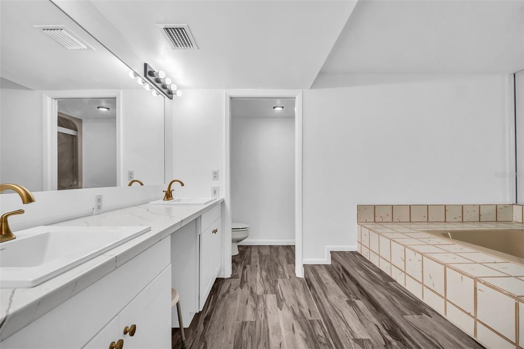 A bathroom features a double vanity with gold faucets, wood-look flooring, and a tiled tub — 55 ROGERS STREET UNIT P5, CLEARWATER, FL