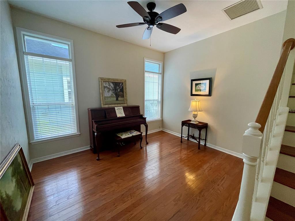 A room with hardwood floors, a piano, a ceiling fan, and a staircase — 10334 SW 51ST LANE, GAINESVILLE, FL