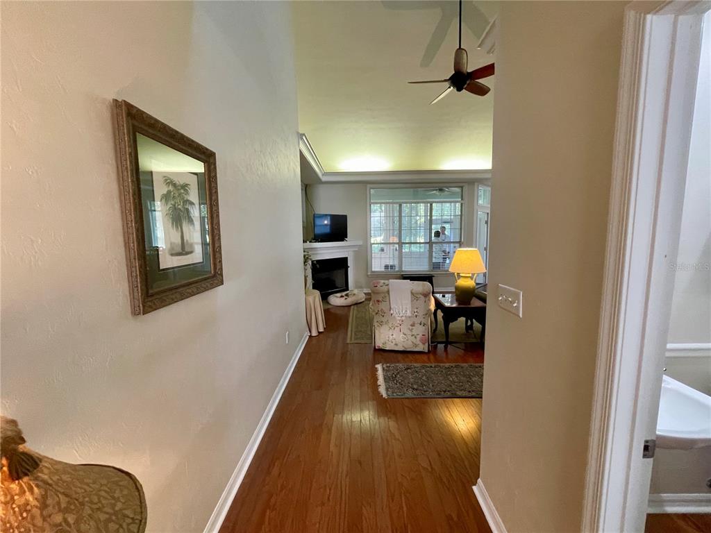 A hallway with hardwood floors leads into a living room featuring a fireplace and windows — 10334 SW 51ST LANE, GAINESVILLE, FL