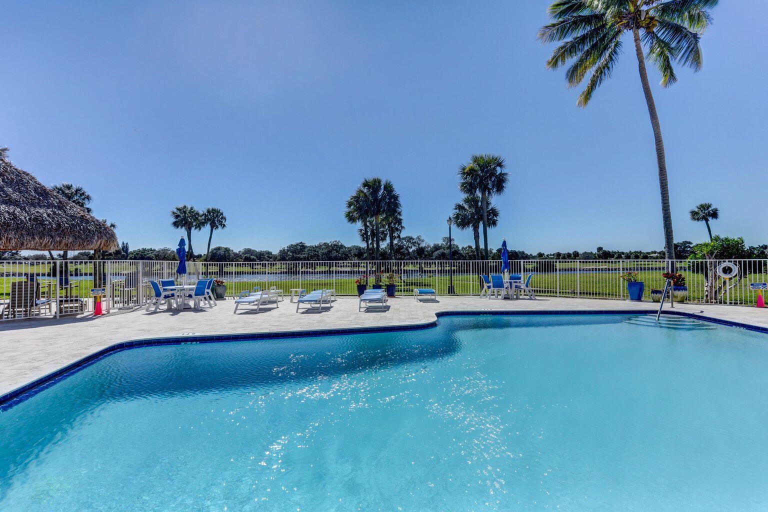 A swimming pool with lounge chairs and palm trees sits behind a white fence — 336 Golfview Road # 203, North Palm Beach FL 33408, NORTH PALM BEACH, FL