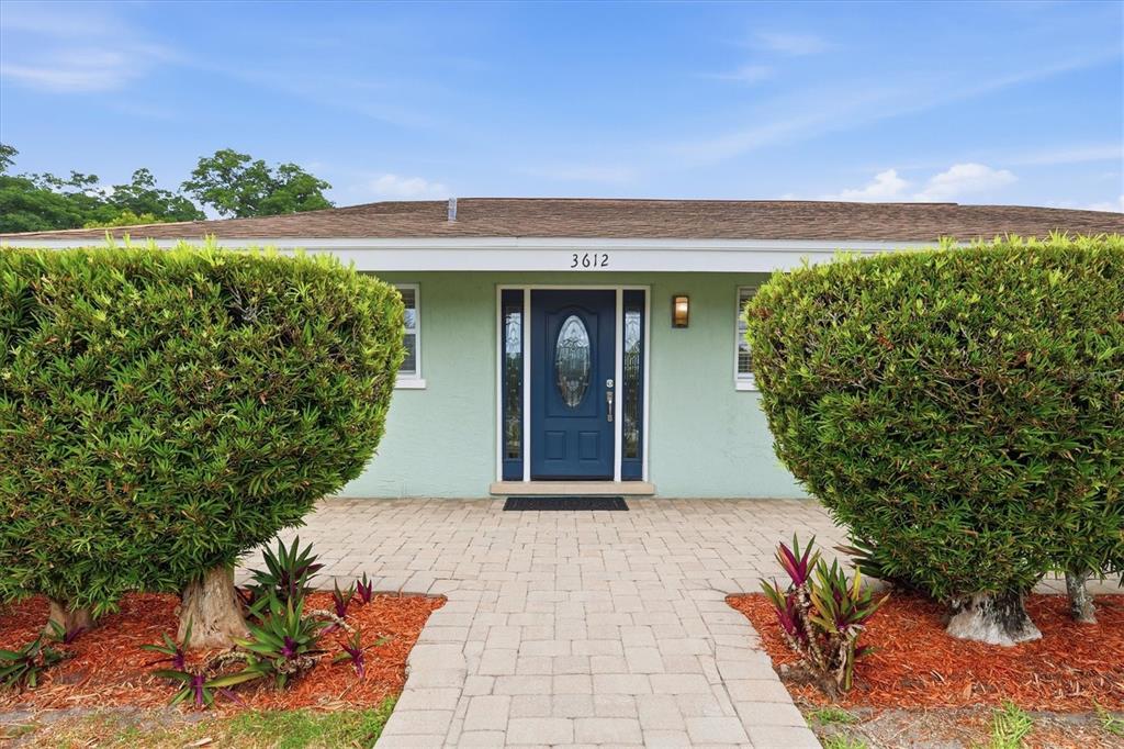 A light green house features a blue front door and a paved walkway between bushes — 3612 S LOCKWOOD RIDGE ROAD, SARASOTA, FL