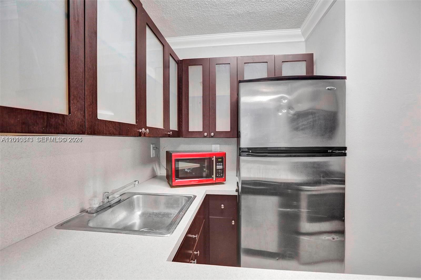This kitchen features dark wood cabinets, a stainless steel refrigerator, and a red microwave — 126 SW 17th Rd # 601, Miami FL 33129, MIAMI, FL