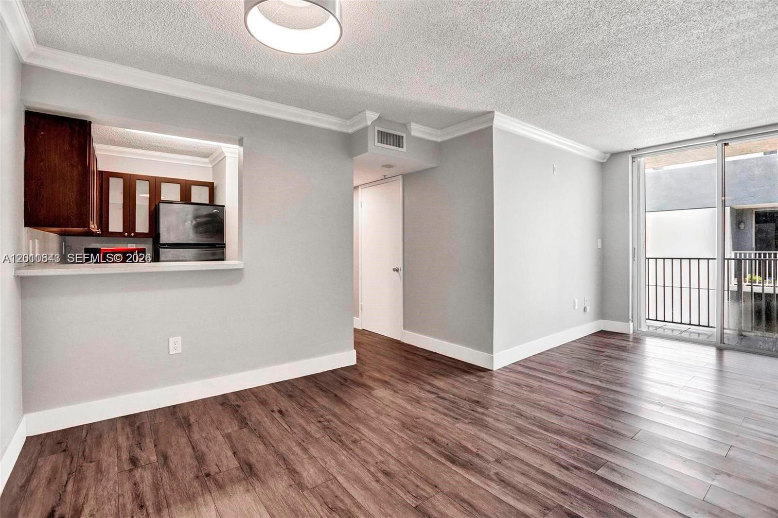 An unfurnished living room features wood-look flooring, a pass-through kitchen window, and a sliding glass door — 126 SW 17th Rd # 601, Miami FL 33129, MIAMI, FL