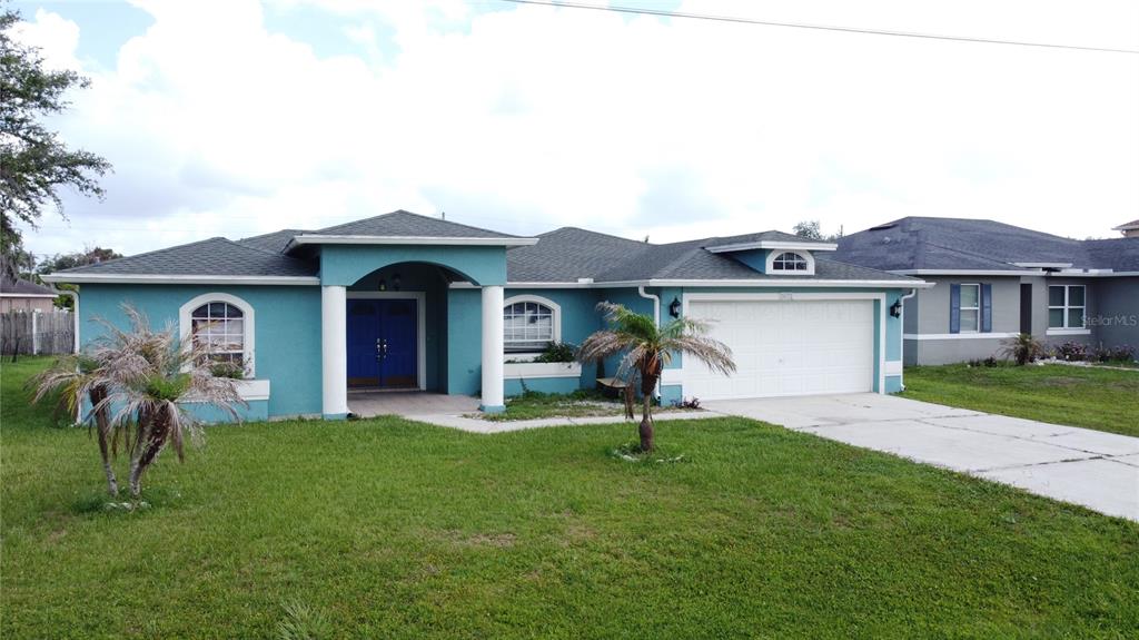 A teal single-story house with a white garage, arched windows, and a covered front entrance — 413 FLAMINGO CT, POINCIANA, FL