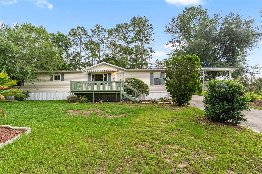 A single-story manufactured home features light siding, a green wooden deck, and a carport — 10831 NW 10TH PLACE, OCALA, FL