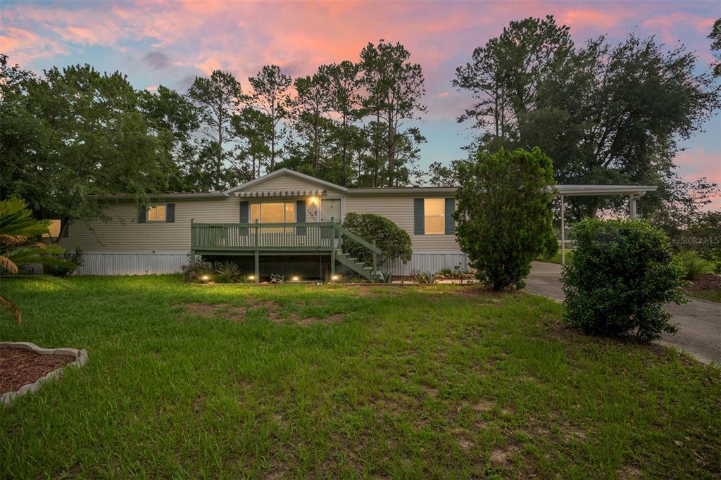 A single-story manufactured home with a wooden deck and carport sits on a grassy lot — 10831 NW 10TH PLACE, OCALA, FL