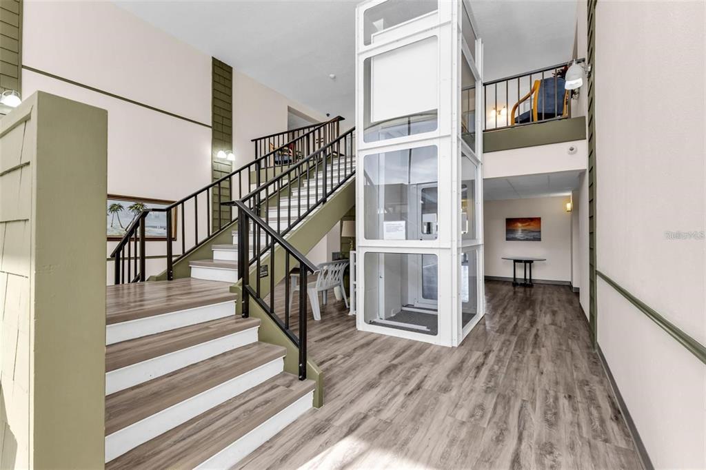 An indoor staircase and a glass elevator are located in a modern, open-concept building lobby — 21267 GERTRUDE AVENUE UNIT 112, PORT CHARLOTTE, FL