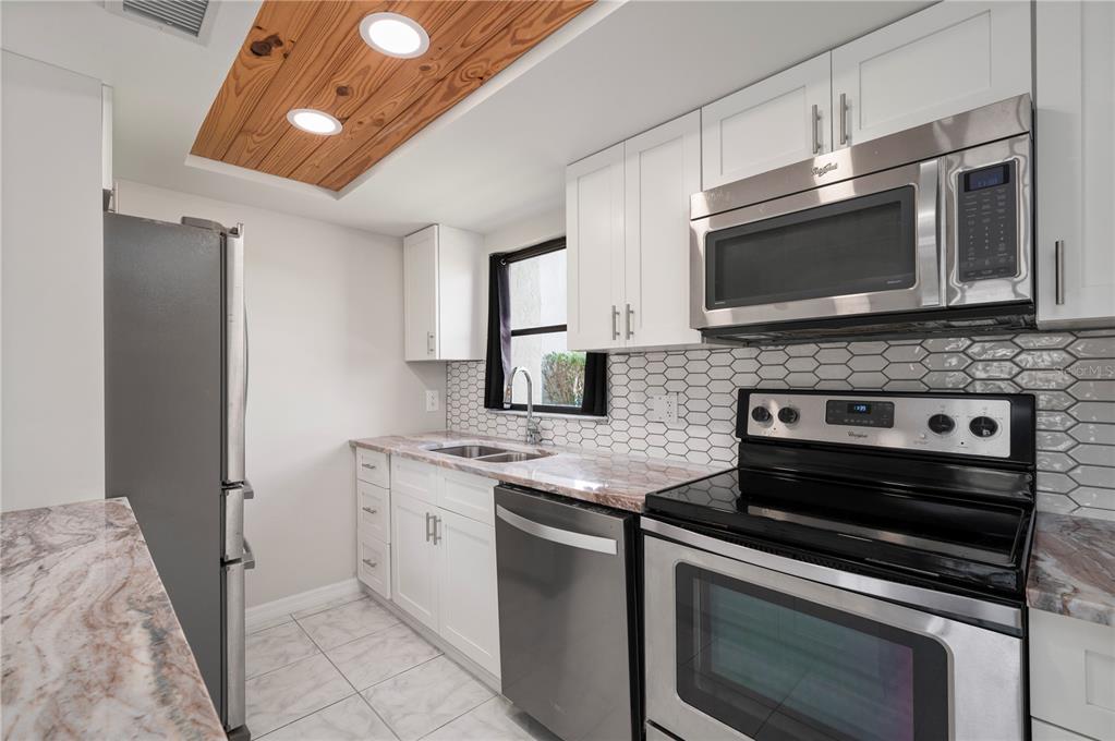 A kitchen features white cabinets, stainless steel appliances, marble-look countertops, and a wood-paneled ceiling — 3230 WHITE IBIS COURT UNIT A1-2, PUNTA GORDA, FL