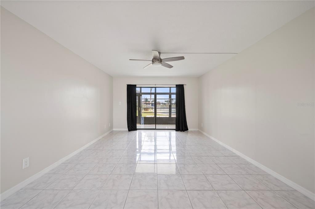 An empty room features light-colored tile flooring, a ceiling fan, and sliding glass doors — 3230 WHITE IBIS COURT UNIT A1-2, PUNTA GORDA, FL