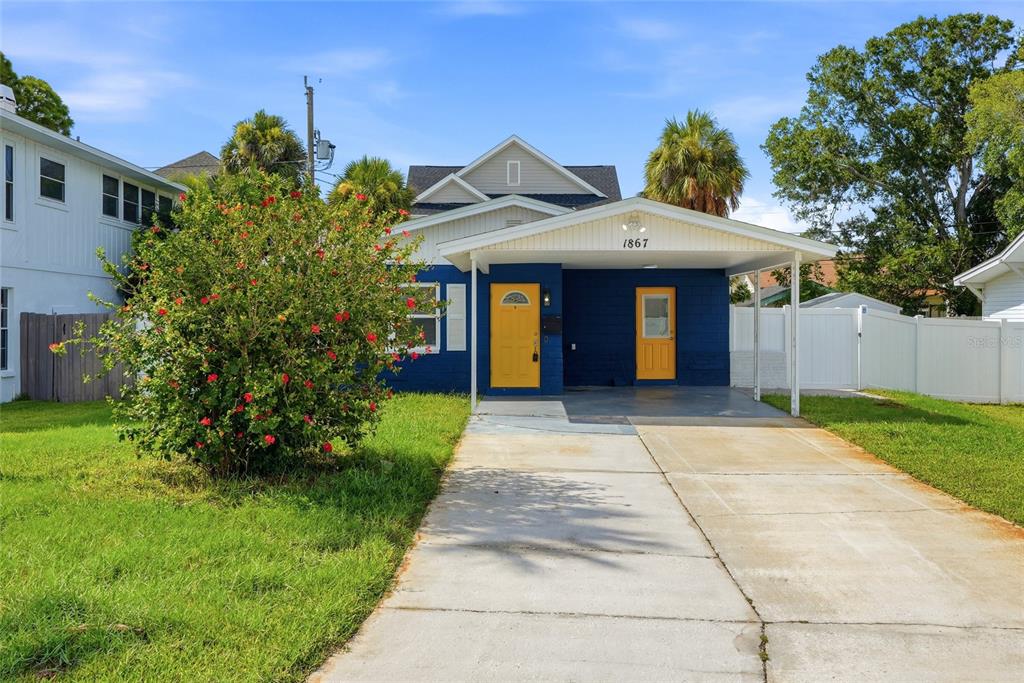 A blue house with a yellow front door and a carport sits behind a driveway — 1867 MICHIGAN AVENUE NE, ST PETERSBURG, FL