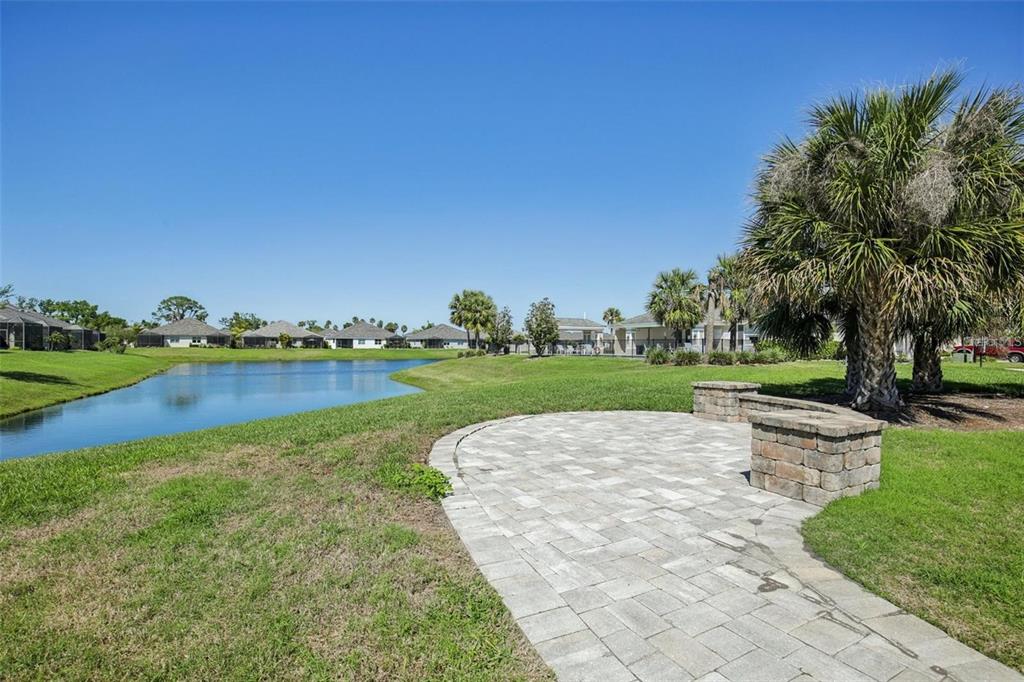 A paved patio with a stone fire pit overlooks a pond and residential homes — 2946 TRUSTEE AVENUE, SARASOTA, FL