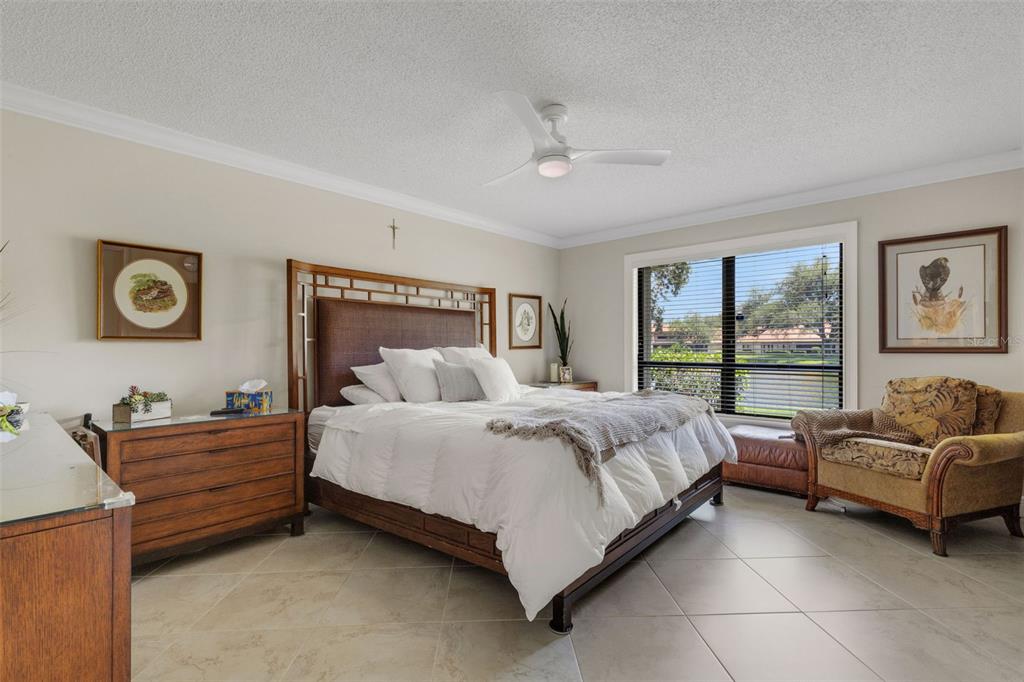 A bedroom features a wooden bed frame, tile flooring, a ceiling fan, and a window — 3902 WILSHIRE DRIVE UNIT 98, SARASOTA, FL