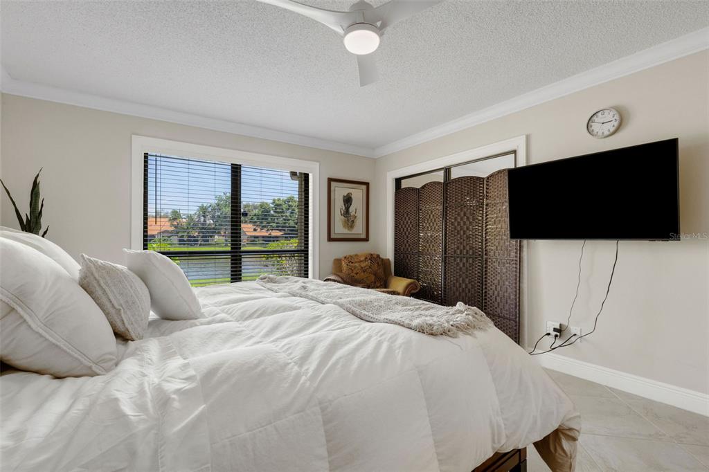 A bedroom features a bed with white bedding, a wall-mounted television, and a window view — 3902 WILSHIRE DRIVE UNIT 98, SARASOTA, FL
