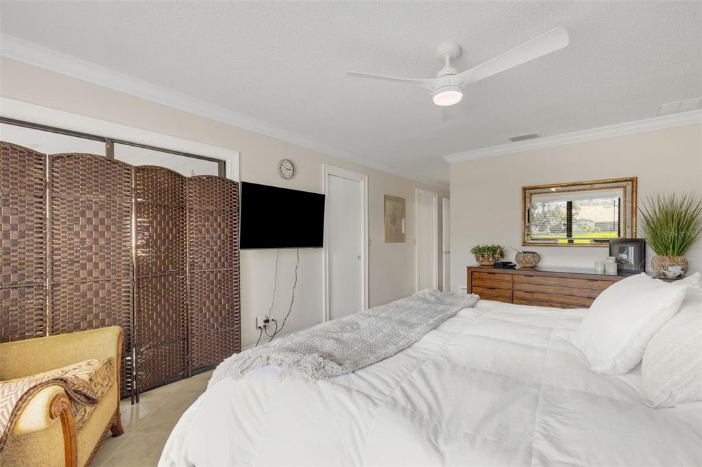A bedroom features a white bed, a wooden dresser, a ceiling fan, and a room divider — 3902 WILSHIRE DRIVE UNIT 98, SARASOTA, FL