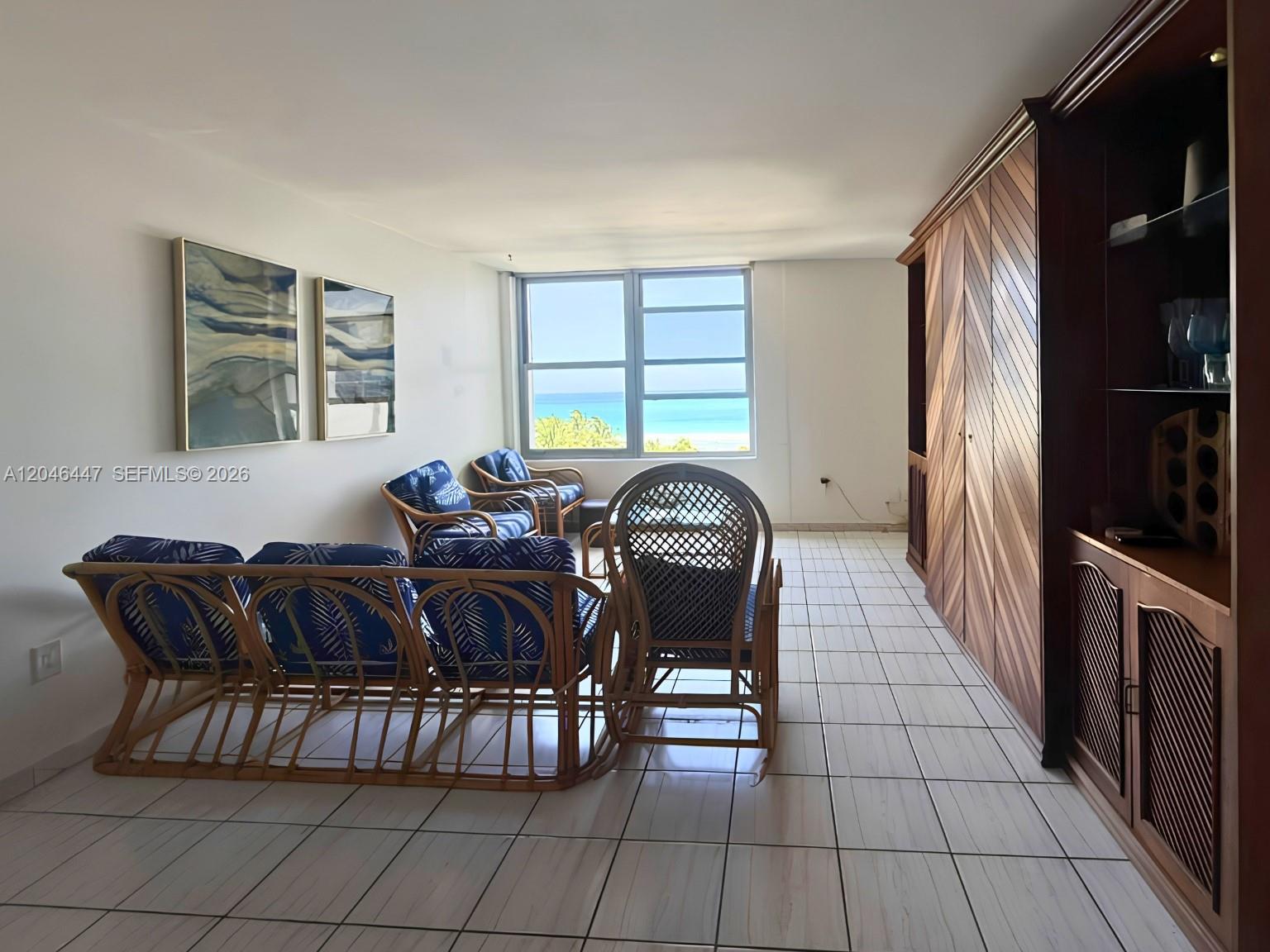 A living room features rattan furniture, tile floors, built-in cabinetry, and a view of the ocean — 2899 Collins Ave # 905, Miami Beach FL 33140, MIAMI BEACH, FL