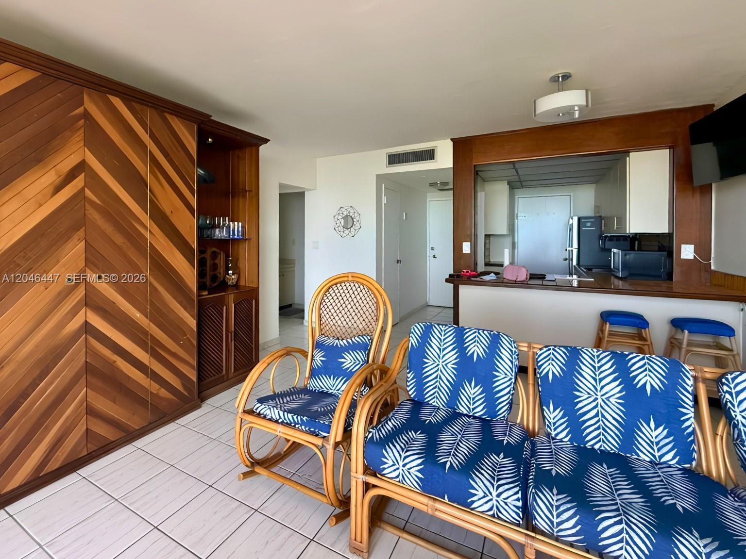 A living room features wicker furniture with blue palm-print cushions and a large wooden cabinet — 2899 Collins Ave # 905, Miami Beach FL 33140, MIAMI BEACH, FL