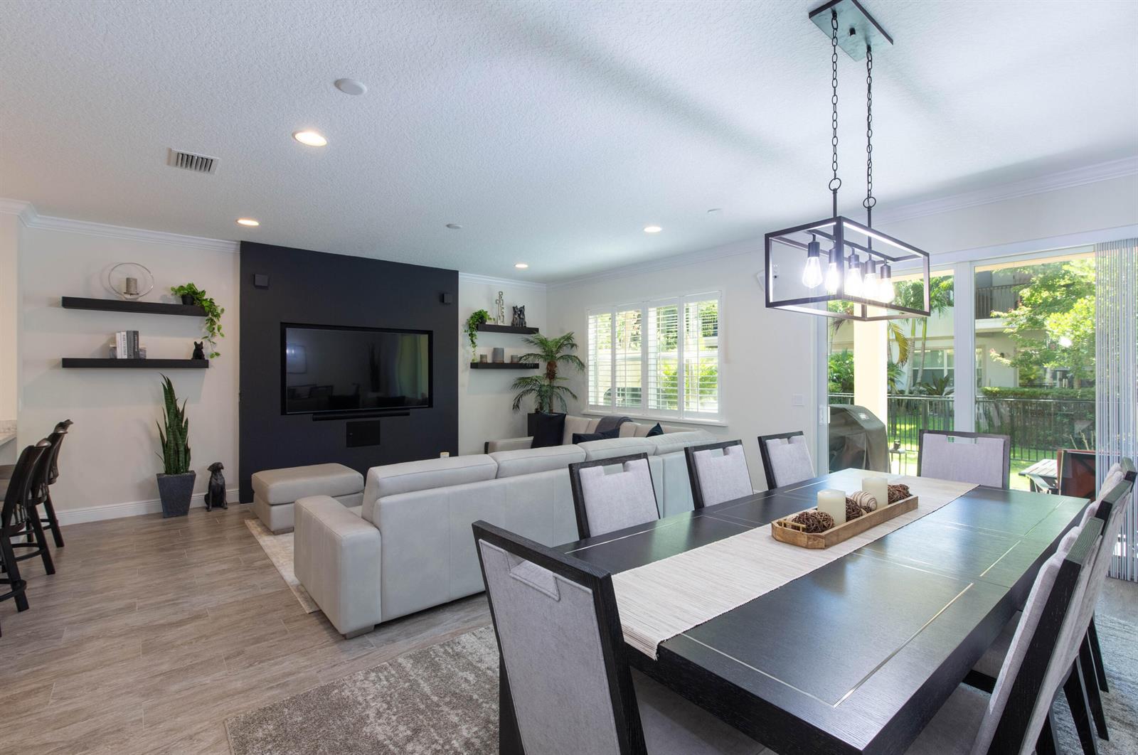 An open-concept living and dining area features a black accent wall, sectional sofa, and chandelier — 168 Crape Myrtle Lane, Wellington FL 33414, WELLINGTON, FL