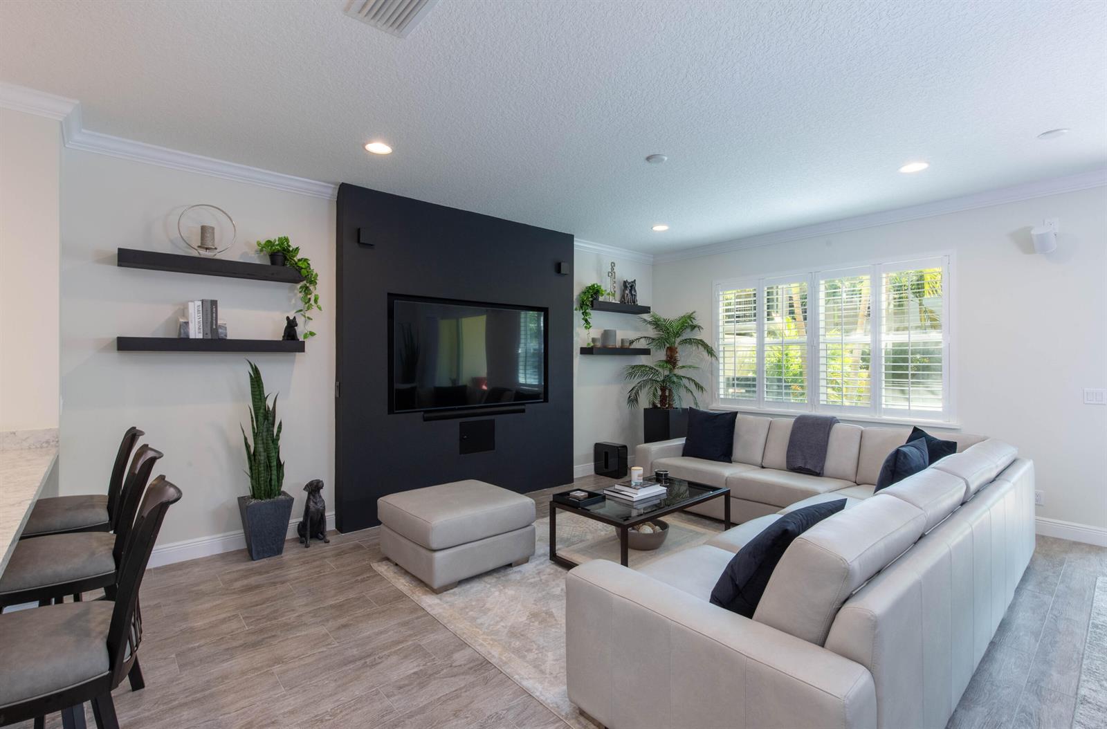 A living room features a black accent wall with a television, sectional sofa, and shelving — 168 Crape Myrtle Lane, Wellington FL 33414, WELLINGTON, FL