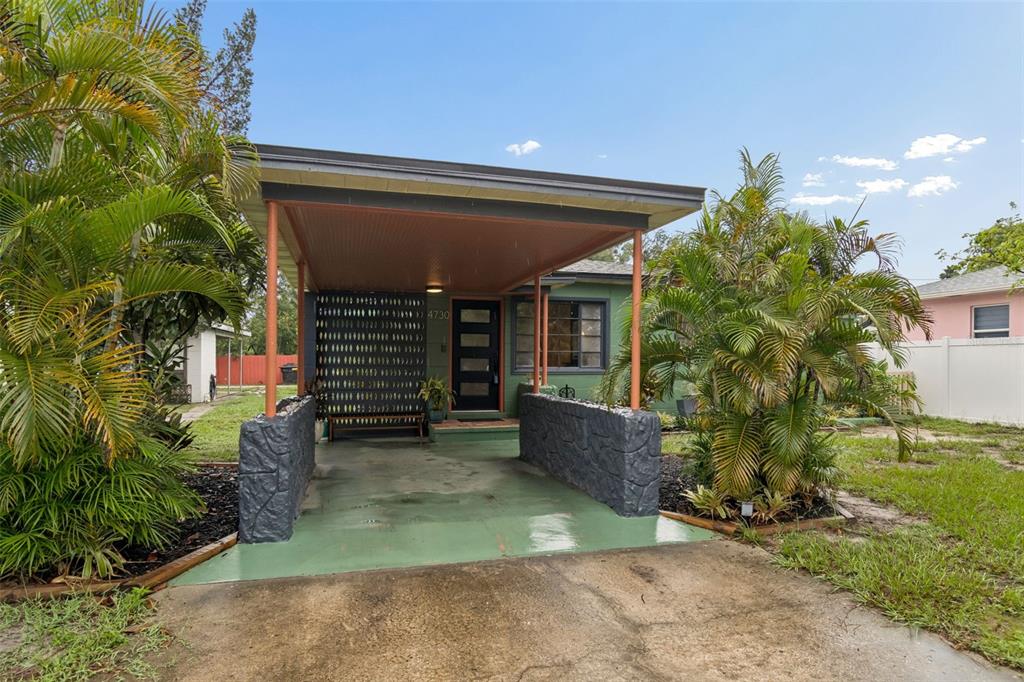 A green house features a covered carport with orange ceiling and dark stone pillars — 4730 15TH AVENUE N, ST PETERSBURG, FL