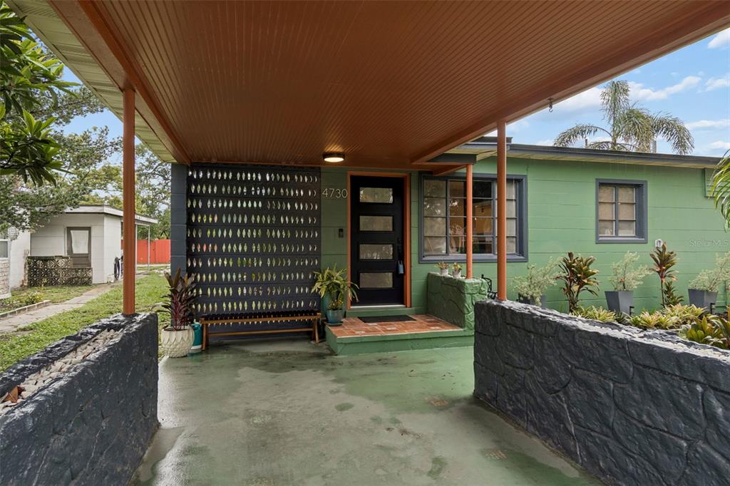 A green house exterior features a covered carport with a black stone wall and door — 4730 15TH AVENUE N, ST PETERSBURG, FL