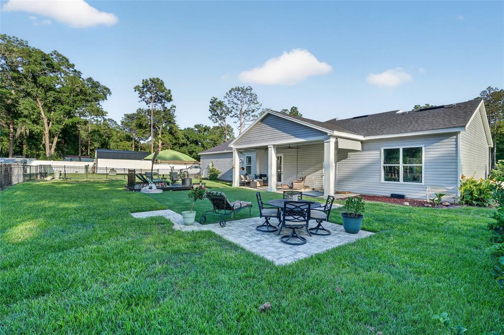 A backyard features a stone patio with outdoor furniture, a covered porch, and a lawn — 13825 SW 51ST LANE, OCALA, FL