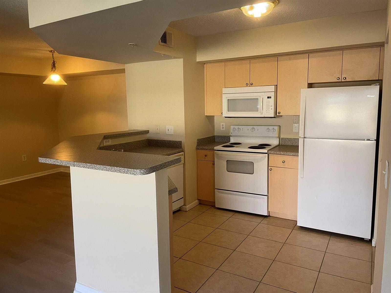 A kitchen with light wood cabinets, white appliances, and a breakfast bar overlooking a room — 3605 NW Adriatic Lane # 103, Jensen Beach FL 34957, JENSEN BEACH, FL
